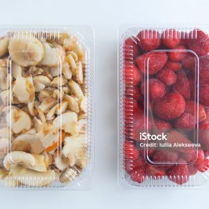 Frozen strawberries and champignons in a transparent plastic container on a white background.