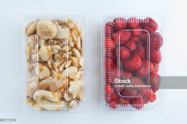 Frozen strawberries and champignons in a transparent plastic container on a white background.